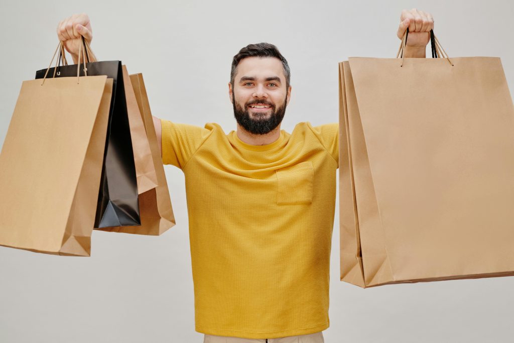 home Happy man in yellow shirt holding multiple shopping bags, expressing joy of shopping.