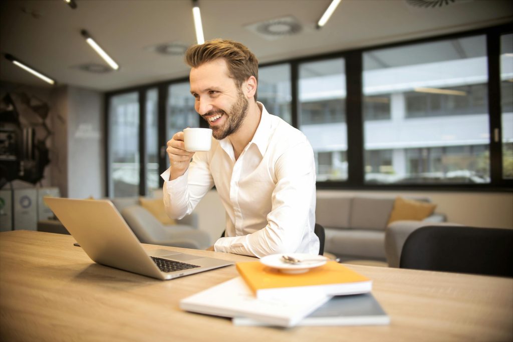home Man enjoying a coffee break while working in a modern office with laptop and books.